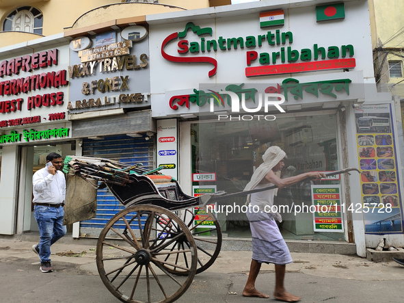 A hand-pulled rickshaw is passing next to an International Bus transport office in Kolkata, India, on July 21, 2024. International Bus Servi...