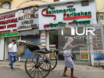 A hand-pulled rickshaw is passing next to an International Bus transport office in Kolkata, India, on July 21, 2024. International Bus Servi...