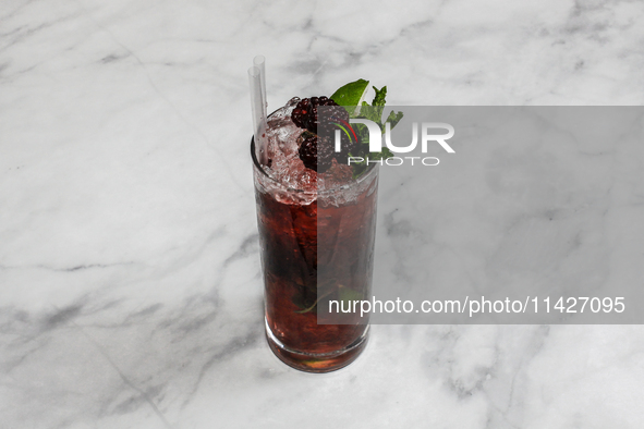 A cocktail ''Blackberry Mojito'' is sitting on a bright background. 