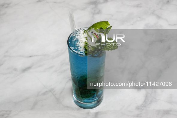 A cocktail ''Blue Hawaiian Mojito'' is sitting on a bright background. 