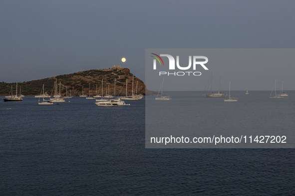 The Full Buck Moon rises behind the ancient Greek Temple of Poseidon on Cape Sounion in Greece with ships in the sea, on July 20, 2024 