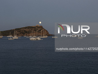 The Full Buck Moon rises behind the ancient Greek Temple of Poseidon on Cape Sounion in Greece with ships in the sea, on July 20, 2024 (