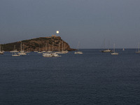 The Full Buck Moon rises behind the ancient Greek Temple of Poseidon on Cape Sounion in Greece with ships in the sea, on July 20, 2024 (