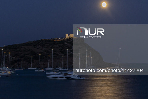 The Full Buck Moon rises behind the ancient Greek Temple of Poseidon on Cape Sounion in Greece with ships in the sea, on July 20, 2024 