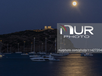 The Full Buck Moon rises behind the ancient Greek Temple of Poseidon on Cape Sounion in Greece with ships in the sea, on July 20, 2024 (