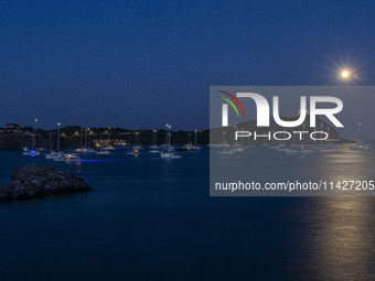 The Full Buck Moon rises behind the ancient Greek Temple of Poseidon on Cape Sounion in Greece with ships in the sea, on July 20, 2024 (