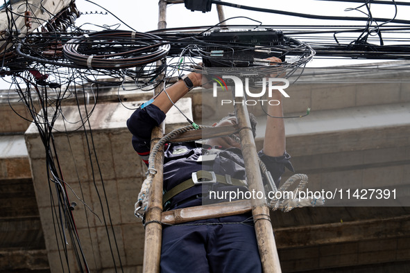 A municipal worker is standing on a bamboo ladder to perform maintenance on a mess of electrical wires in Bangkok, Thailand, on July 22, 202...