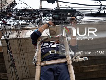 A municipal worker is standing on a bamboo ladder to perform maintenance on a mess of electrical wires in Bangkok, Thailand, on July 22, 202...