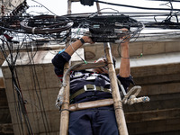 A municipal worker is standing on a bamboo ladder to perform maintenance on a mess of electrical wires in Bangkok, Thailand, on July 22, 202...