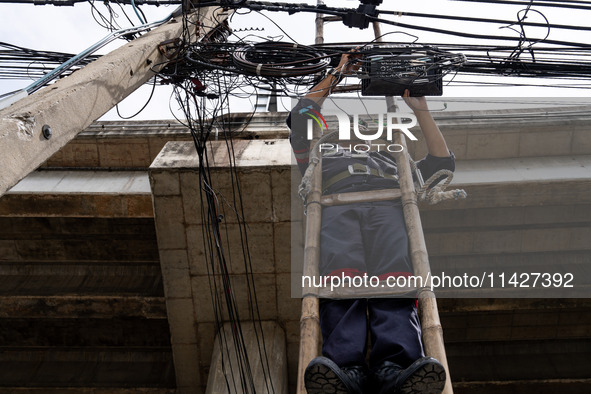 A municipal worker is standing on a bamboo ladder to perform maintenance on a mess of electrical wires in Bangkok, Thailand, on July 22, 202...