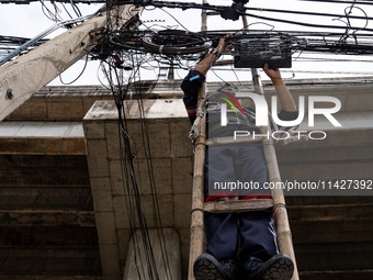 A municipal worker is standing on a bamboo ladder to perform maintenance on a mess of electrical wires in Bangkok, Thailand, on July 22, 202...