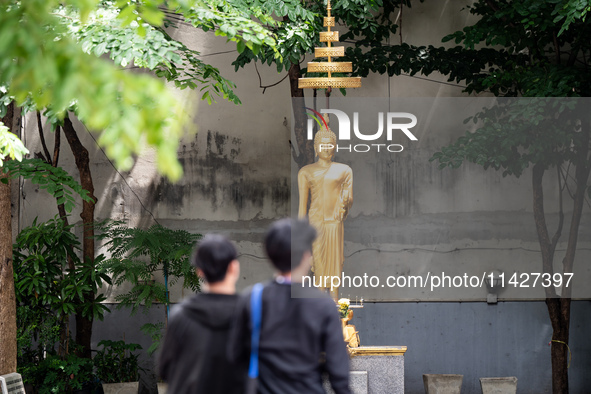 People are walking past a golden Buddha statue in Bangkok, Thailand, on July 22, 2024 