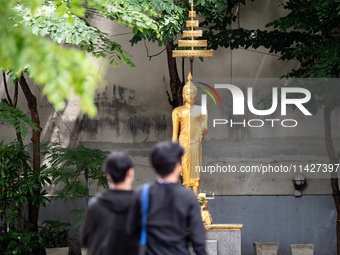 People are walking past a golden Buddha statue in Bangkok, Thailand, on July 22, 2024 (