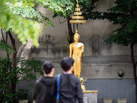 People are walking past a golden Buddha statue in Bangkok, Thailand, on July 22, 2024 (