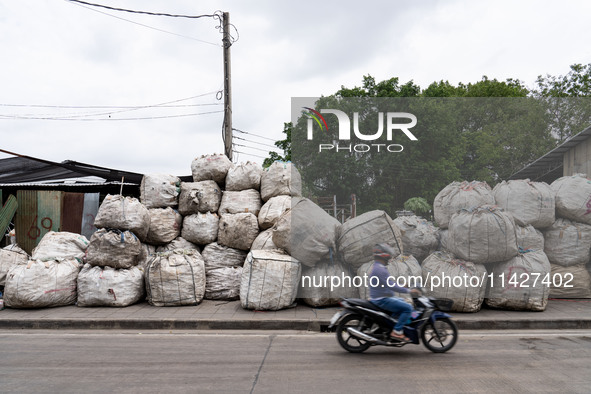 Someone is driving a motorcycle past large bags of waste sitting outside of a sorting facility in Bangkok, Thailand, on July 22, 2024 