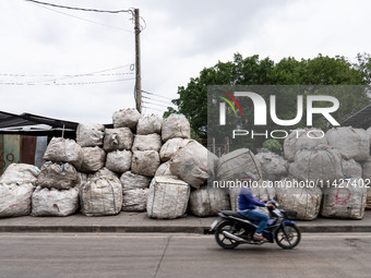 Someone is driving a motorcycle past large bags of waste sitting outside of a sorting facility in Bangkok, Thailand, on July 22, 2024 (