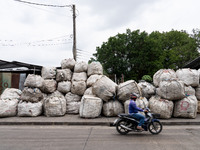 Someone is driving a motorcycle past large bags of waste sitting outside of a sorting facility in Bangkok, Thailand, on July 22, 2024 (