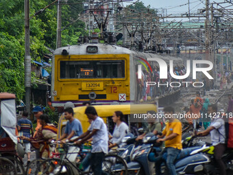 People are crossing a railway track as a train is leaving the station in Kolkata, India, on July 22, 2024. It is expected that the railway i...