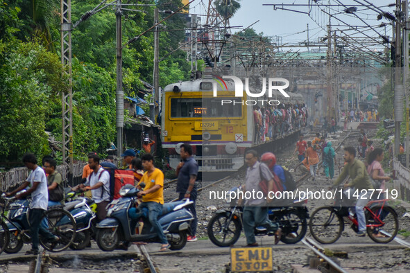 People are crossing a railway track as a train is leaving the station in Kolkata, India, on July 22, 2024. It is expected that the railway i...