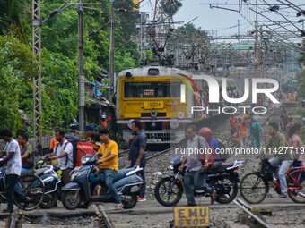 People are crossing a railway track as a train is leaving the station in Kolkata, India, on July 22, 2024. It is expected that the railway i...