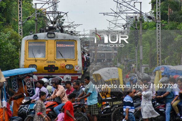 People are crossing a railway track as a train is leaving the station in Kolkata, India, on July 22, 2024. It is expected that the railway i...