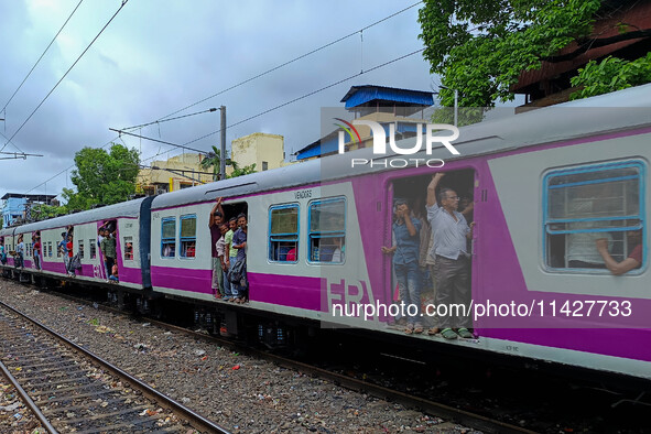 People are hanging from a train door as they are traveling in a local train in Kolkata, India, on July 22, 2024. It is expected that the rai...