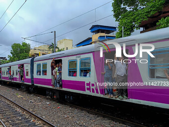 People are hanging from a train door as they are traveling in a local train in Kolkata, India, on July 22, 2024. It is expected that the rai...