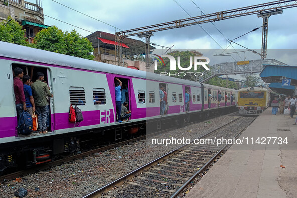 People are hanging from a train door as they are traveling in a local train in Kolkata, India, on July 22, 2024. It is expected that the rai...