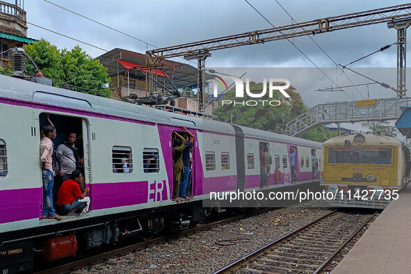 People are hanging from a train door as they are traveling in a local train in Kolkata, India, on July 22, 2024. It is expected that the rai...