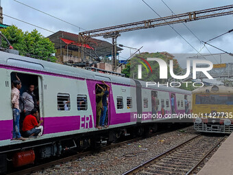 People are hanging from a train door as they are traveling in a local train in Kolkata, India, on July 22, 2024. It is expected that the rai...