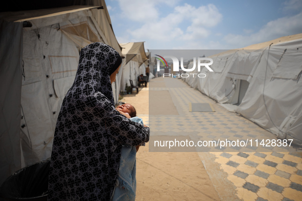 A displaced Palestinian mother is holding her baby at the International Medical Corps field hospital, amid the Israel-Hamas conflict, in Dei...