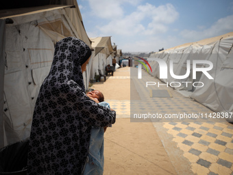 A displaced Palestinian mother is holding her baby at the International Medical Corps field hospital, amid the Israel-Hamas conflict, in Dei...