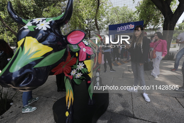 A woman is taking a photo of a fiberglass cow painting by an artist during the inauguration of the 'Cowparade Mexico 2024' on Avenida Reform...