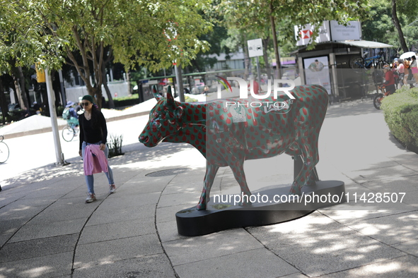 A woman is walking next to a fiberglass cow painted by an artist during the inauguration of the 'Cowparade Mexico 2024' on Avenida Reforma i...