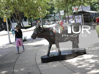 A woman is walking next to a fiberglass cow painted by an artist during the inauguration of the 'Cowparade Mexico 2024' on Avenida Reforma i...