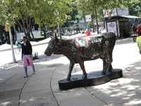 A woman is walking next to a fiberglass cow painted by an artist during the inauguration of the 'Cowparade Mexico 2024' on Avenida Reforma i...