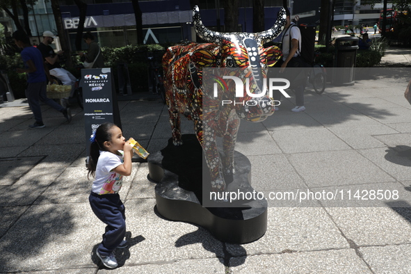 A child is walking in front of a fiberglass cow painted by an artist during the inauguration of the 'Cowparade Mexico 2024' on Avenida Refor...