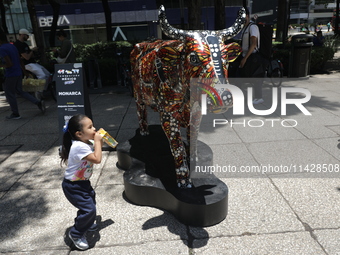 A child is walking in front of a fiberglass cow painted by an artist during the inauguration of the 'Cowparade Mexico 2024' on Avenida Refor...