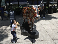 A child is walking in front of a fiberglass cow painted by an artist during the inauguration of the 'Cowparade Mexico 2024' on Avenida Refor...