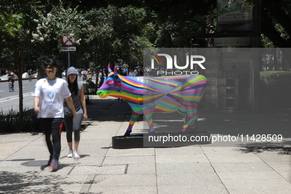 Persons are walking next to a fiberglass cow painted by an artist during the inauguration of the 'Cowparade Mexico 2024' on Avenida Reforma...