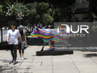 Persons are walking next to a fiberglass cow painted by an artist during the inauguration of the 'Cowparade Mexico 2024' on Avenida Reforma...