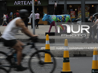 A cyclist is riding in front of a fiberglass cow painted by an artist during the inauguration of the 'Cowparade Mexico 2024' on Avenida Refo...