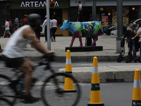 A cyclist is riding in front of a fiberglass cow painted by an artist during the inauguration of the 'Cowparade Mexico 2024' on Avenida Refo...