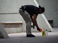 A crime scene investigator is placing an evidence marker at the crime scene where a shell casing is being discovered next to a bottle of liq...