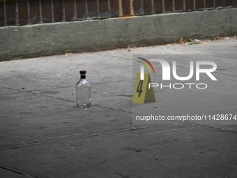 An evidence marker is being placed at the crime scene where a shell casing is being discovered next to a bottle of liquor following an overn...