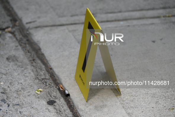 An evidence marker is being placed at the crime scene where a shell casing is being discovered following an overnight fatal shooting in Bron...