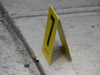 An evidence marker is being placed at the crime scene where a shell casing is being discovered following an overnight fatal shooting in Bron...