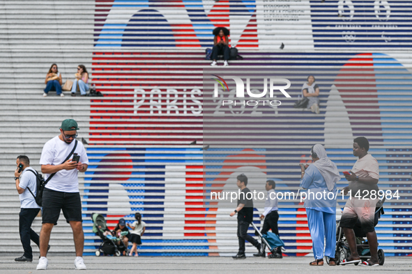 PARIS, FRANCE - JULY 22:   
People gather around the steps of the Grande Arche adorned with Olympic-themed graphics, celebrating the upcomin...