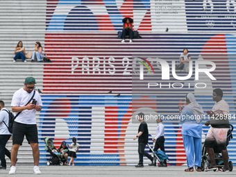 PARIS, FRANCE - JULY 22:   
People gather around the steps of the Grande Arche adorned with Olympic-themed graphics, celebrating the upcomin...