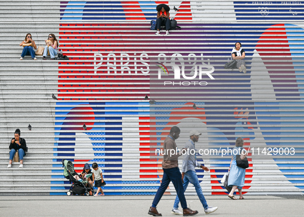 People gather around the steps of the Grande Arche adorned with Olympic-themed graphics, celebrating the upcoming Paris 2024 Olympic Games,...